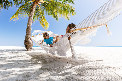 Happy boy and his single mother swinging in hammock on the beach. Copy space.