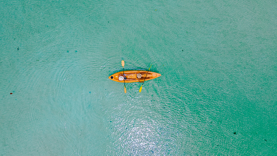 Men and women in a Kayak peddling in the turquoise-colored ocean of the tropical Island of Koh Mak Thailand. men and women in kayaks at a blue ocean and white beach with palm trees