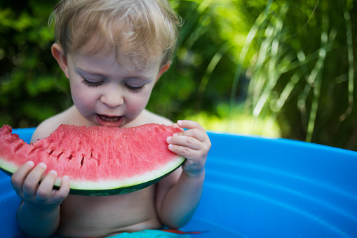 Cute little toddler boy taking a bath in garden and eat watermelon