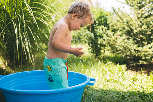 Cute little toddler boy taking a bath in a garden