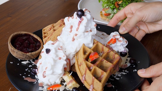 Belgian waffles with cream and berries on breakfast. Rotating plate with hands. A delicious breakfast is essential for your health throughout the day. Close-up. Vegetarian waffles without eggs.