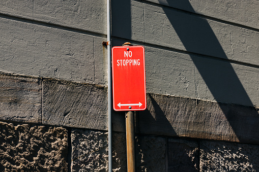 Red metal No stopping sign on a gray metal pole, with a building behind.