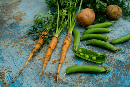 Carrots, green peas, and potatoes on a rusty metal surface. Classic soup set with young vegetables. Rural still life.