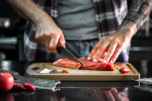 Man cuts beef meat in the kitchen