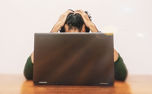 Stressed and Anxious Young Man Holding Face while Looking at Laptop Screen.