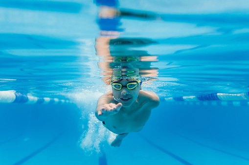 latin child boy swimmer underwater wearing cap and goggles in a swimming training at the Pool in Mexico Latin America