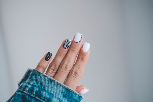 Beautiful female hands with a manicure in a denim jacket. Stylish nail design. Manicure with black and white zebra stripes on the nails.