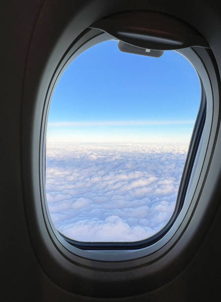 view from the airplane window. beautiful cloudscape with blue sky. wonderful panorama above white clouds as seen through window of an plane. traveling by air concept - window porthole sky cloudscape imagens e fotografias de stock