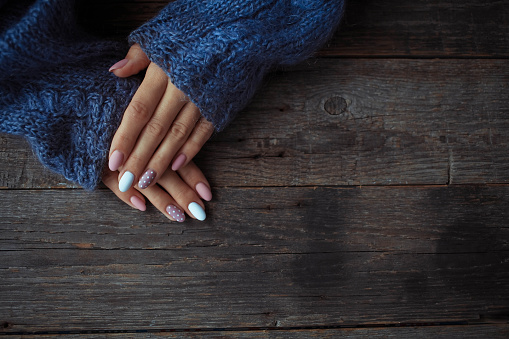 Women is hands with a beautiful manicure, in a knitted sweater on a wooden background in. Autumn trend, polish beige and white polka dots on nails with gel polish, shellac. Close up.