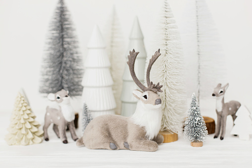 A plastic toy deer looking at the camera in front of some out of focus trees and mountains of paper. Winter landscape. Image with copy sapce.
