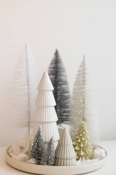 Stylish little Christmas trees on plate on white table. Festive Christmas scene, miniature snowy forest, table setting. Modern minimal scandi decorations. Merry Christmas and Happy Holidays stock photo