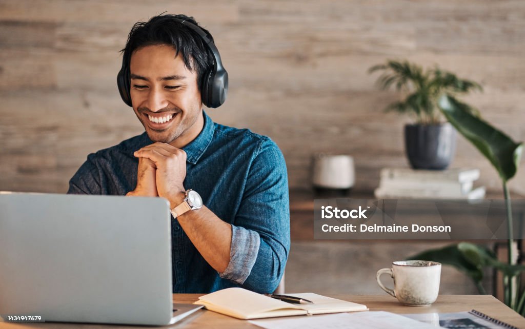 Remote worker, laptop and asian man with headphones streaming online or happy during video conference at desk with wifi. Young freelance entrepreneur working from home listening to audio music Hot Desking Stock Photo