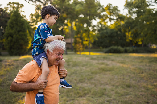 Grandfather carrying his grandson on his shoulders in a public park