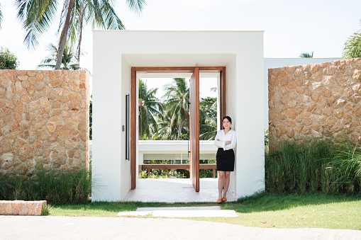 Portrait of smiling hostess of the luxury villa looking at the camera at the entrance of the villa.