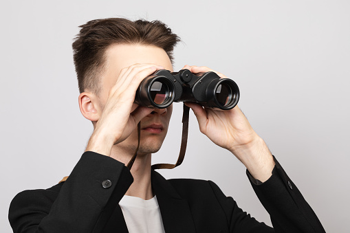 Young Asian businessman looking through binoculars, isolated on white background.