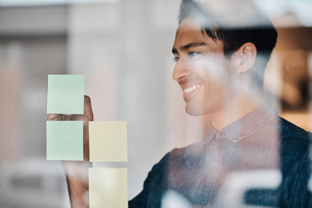 Sticky note, glass board and man planning, working or brainstorming marketing strategy for advertising campaign. Small business owner, entrepreneur or designer work on goals manifestation for startup