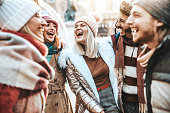 Happy group of friends wearing winter clothes having fun walking on city street - Young people talking and laughing together outside - Friendship concept with guys and girls hanging out on a sunny day