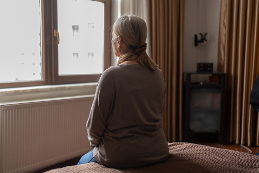 Senior Woman Sitting on Bed and Looking Away from the Window