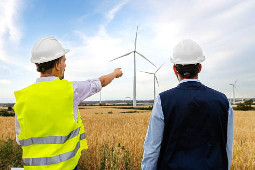 Rear view of foreman explaining to electric engineer news about wind turbine farm.Renewable energy concept.