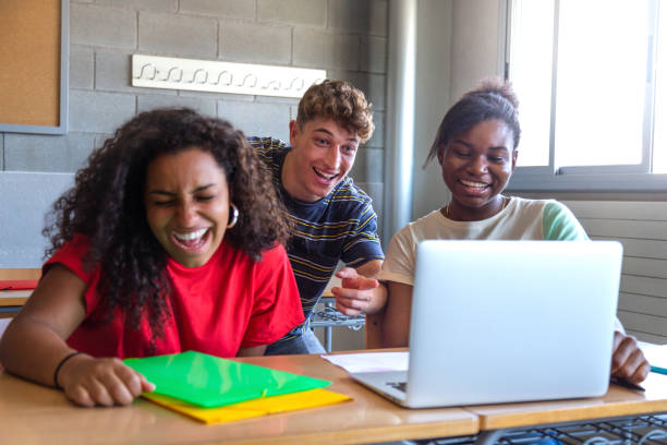 multirassische gruppe von gymnasiasten, die zusammen im unterricht lachen und laptops benutzen, um gemeinsam hausaufgaben zu machen. - child education group of people student stock-fotos und bilder