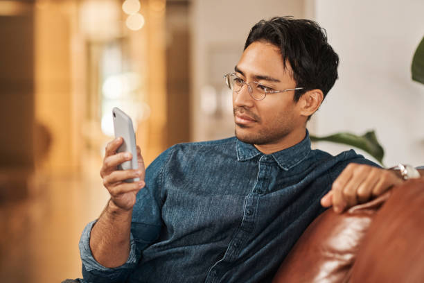 asian man, phone and social media communication app on sofa at home. web internet search, online chat conversation and person read mobile iot sms message on digital tech information technology device - young adult reading newspaper the media imagens e fotografias de stock