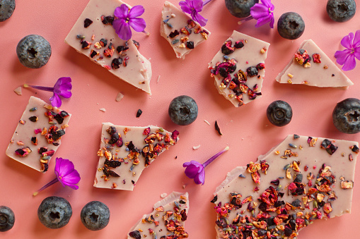 crushed pink chocolate with blueberries and phloxes flowers. Broken bars with nuts and sublimated raspberry on pink -tasty background