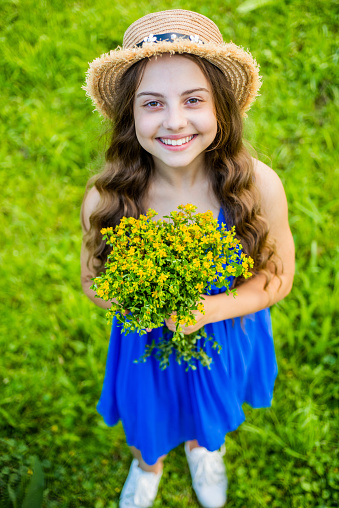 Little girl with a bouquet of daisies in summer on a natural background. Happy child,panama hat for sun protection. International Children's Day. Copy space. Authenticity, rural life, eco-friendly