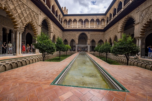 Seville, Spain – June 21, 2022: The Alcazar palace mudejar inner garden decorated with trees and columns in Seville, Spain