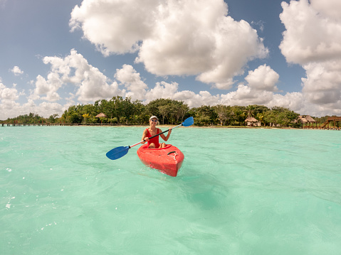 Rear view of woman paddling on red canoe in peaceful blue lagoon in Mexico