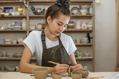 Beautiful teenage girl playing with modeling clay in pottery workshop. Craft and clay art. Children's creativity. Arts education