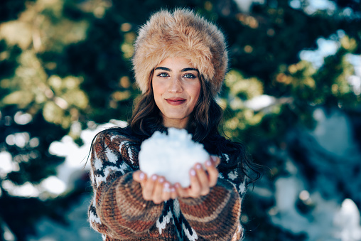 Young woman enjoying the snowy mountains in winter, in Sierra Nevada, Granada, Spain. Female wearing winter clothes playing with snow.