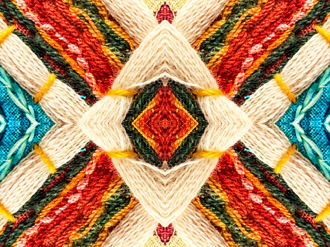 A centered symmetrical pattern. of woven fabric. The colorful design features strands of wool thread.  The yarn reveals a lot of texture.