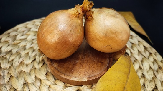 two onions on a wooden plate with a rattan base and a black background for cooking or kitchen purposes