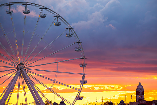 Ferris Wheel and illuminations in amusement park during scenic sunset with dramatic sky clouds and flying birds