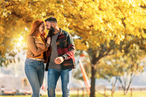 Young happy couple looking at each other while holding hands and walking in autumn park.