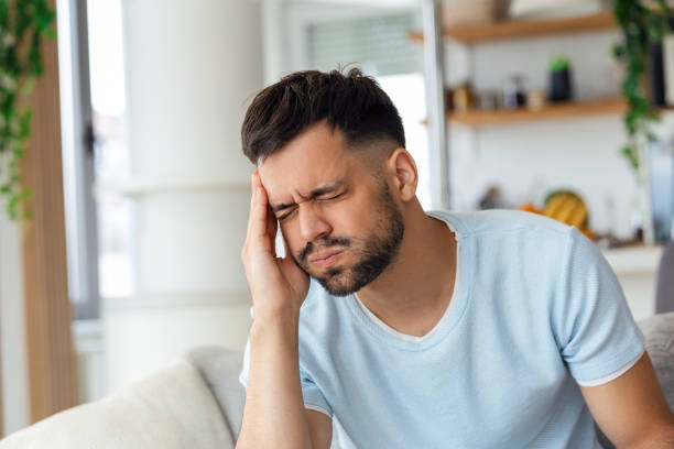 istock Unpleasant pain. Sad unhappy handsome man sitting on the sofa and holding his forehead while having headache 1435001672