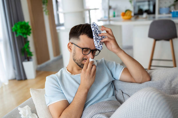 mężczyzna czuje się źle, siedzi na kanapie z bólem głowy i nakłada torbę na lód - ice pack ice headache bag zdjęcia i obrazy z banku zdjęć