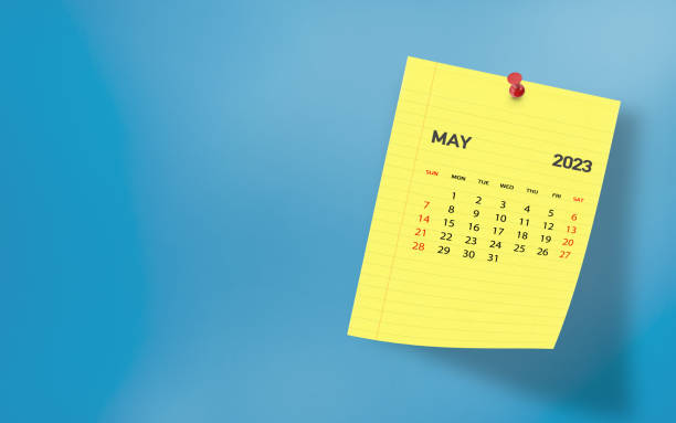 May 2023 calendar on a yellow notepaper page pinned on wall against blue background. High resolution and copy space for all your crop needs.