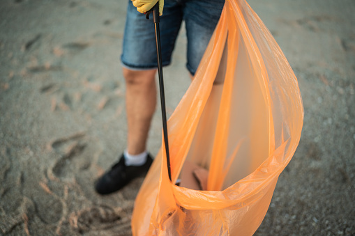 Close-up of recycler putting trash on a plastic bag at beach