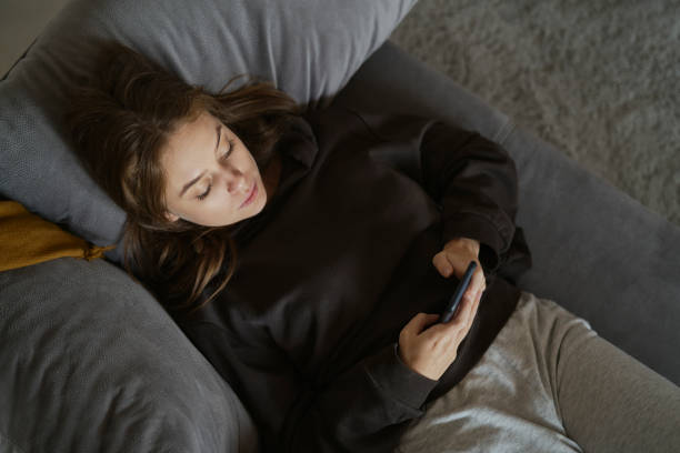 istock Caucasian woman lying down on the couch and using mobile phone 1435005547