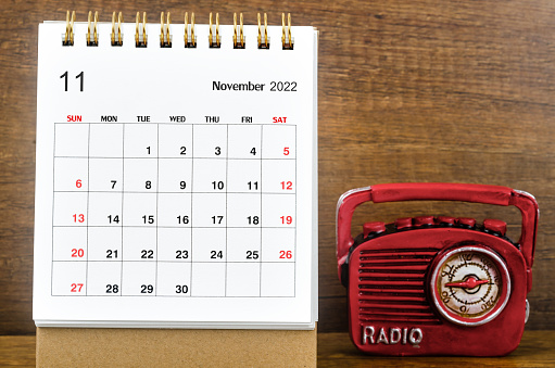 November 2022 Monthly desk calendar for the organizer to plan 2022 year with a vintage red radio against a wooden table background.