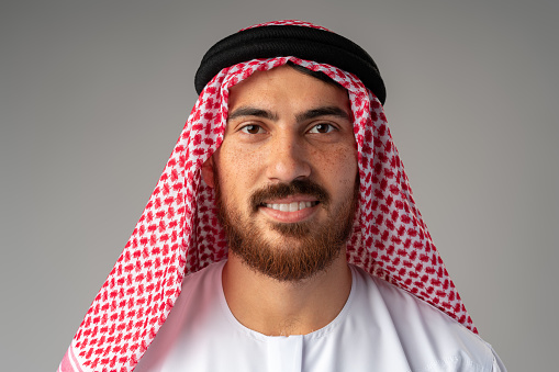Portrait of smiling young Arab man on gray background close up