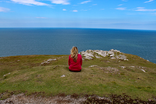 A woman sits on top of the Great Orme in Llandudno, North Wales, and looks out to sea whilst contemplating. The woman is alone with her thoughts, this is good for both her physical wellbeing and her mental health.