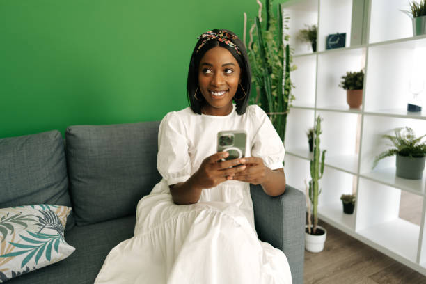 istock Young african woman sitting on couch at home and using smartphone 1435009201