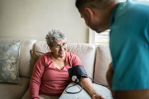 Nurse talking while measuring the pressure of senior woman in the living room in a nursing home