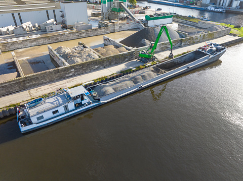 Freight ship barge loaded with sand and stone unloaded at a plant in Meppel, Netherlands. Overhead drone shot.