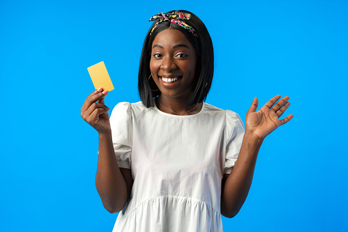 Young african woman holding credit card in hand against blue background in studio