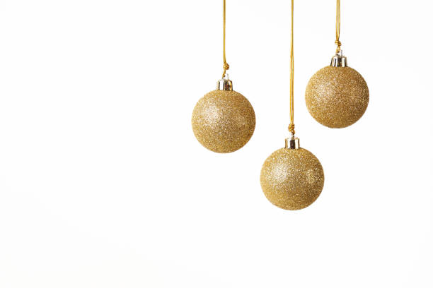 three golden Christmas balls with glitter hanging in front of a white background stock photo