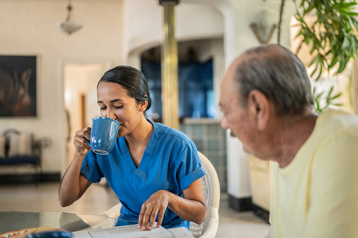 Mid adult nurse drinking while playing with crosswords with senior man on breakfast at home