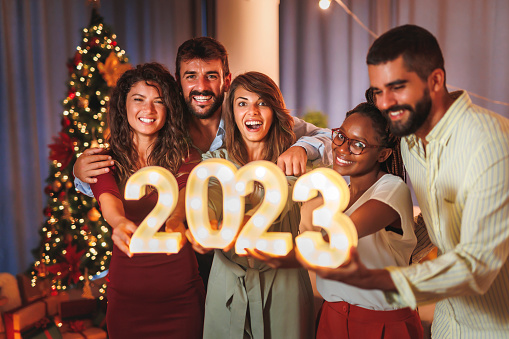 Group of young friends having fun at New Years Eve party, holding illuminative numbers 2023 representing the upcoming New Year